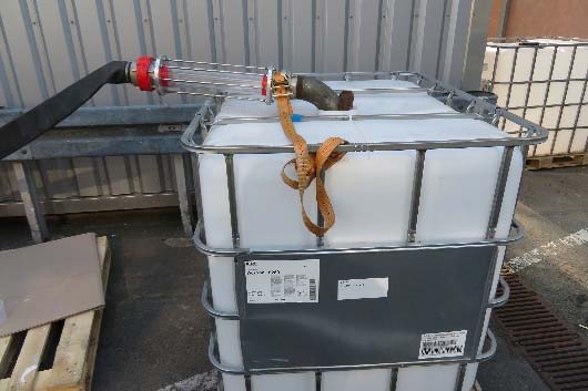 Ein großer weißer Kunststoffbehälter mit einem oben angebrachten Schlauch, der mit einem Riemen außen auf einer Betonoberfläche befestigt ist, ideal für den industriellen Einsatz in Spülverfahren.