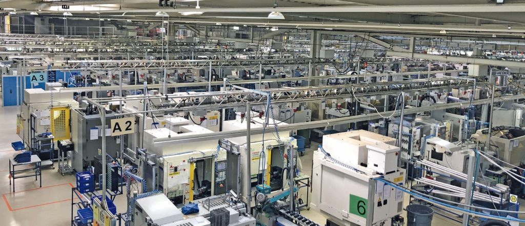 Eine große, geordnete Fabrikhalle mit verschiedenen Maschinen und Geräten, mit zahlreichen Arbeitsplätzen und Rohrleitungen über Kopf, optimiert für Industriestandards.