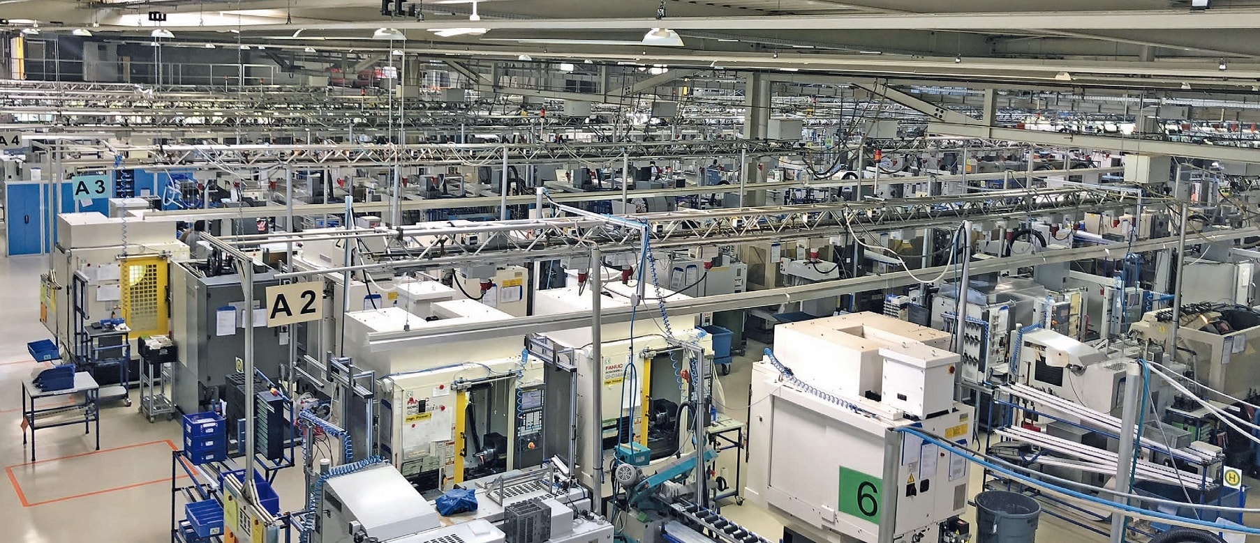 Eine große, geordnete Fabrikhalle mit verschiedenen Maschinen und Geräten, mit zahlreichen Arbeitsplätzen und Rohrleitungen über Kopf, optimiert für Industriestandards.