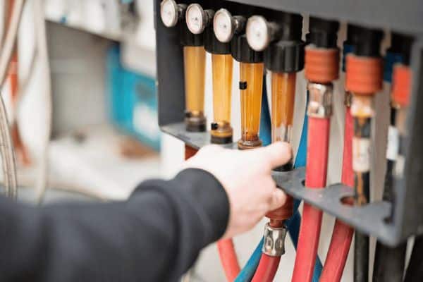 Nahaufnahme einer Person, die Schläuche und Druckmessgeräte an einem mechanischen Industriegerät einstellt.